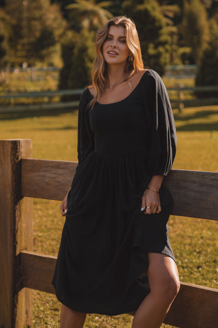 Woman in a black dress standing by a wooden fence in a field