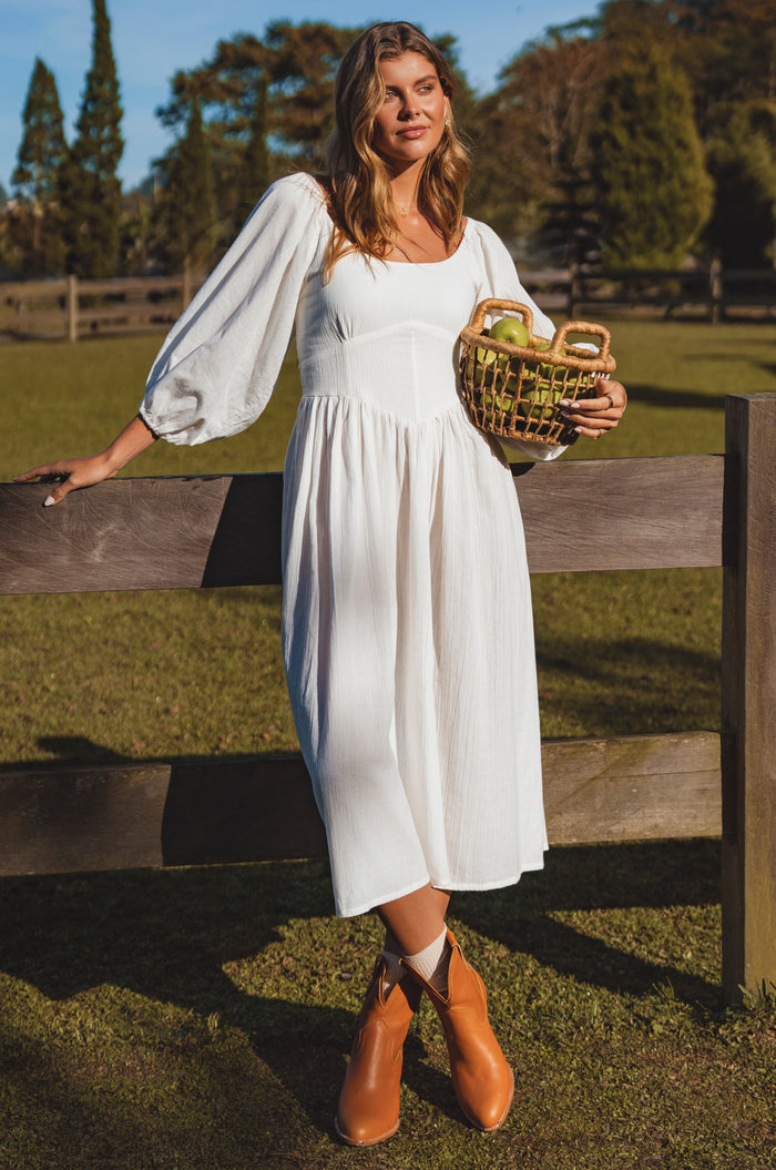Woman in a white dress holding a basket by a wooden fence outdoors