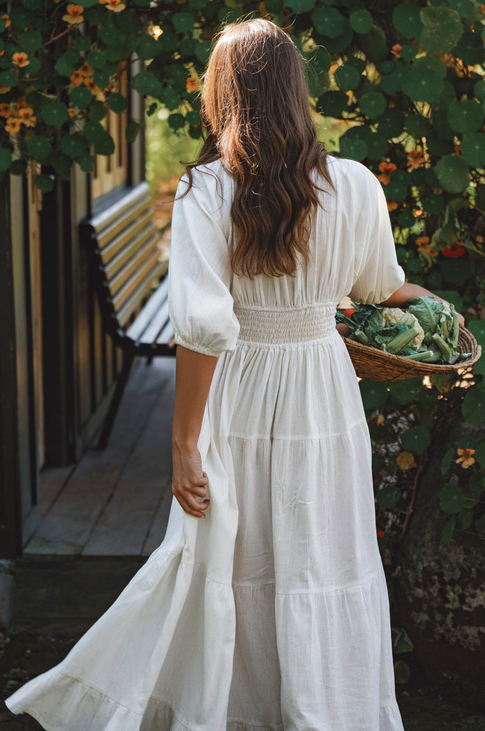 Woman in a white dress holding a basket of vegetables in an outdoor setting
