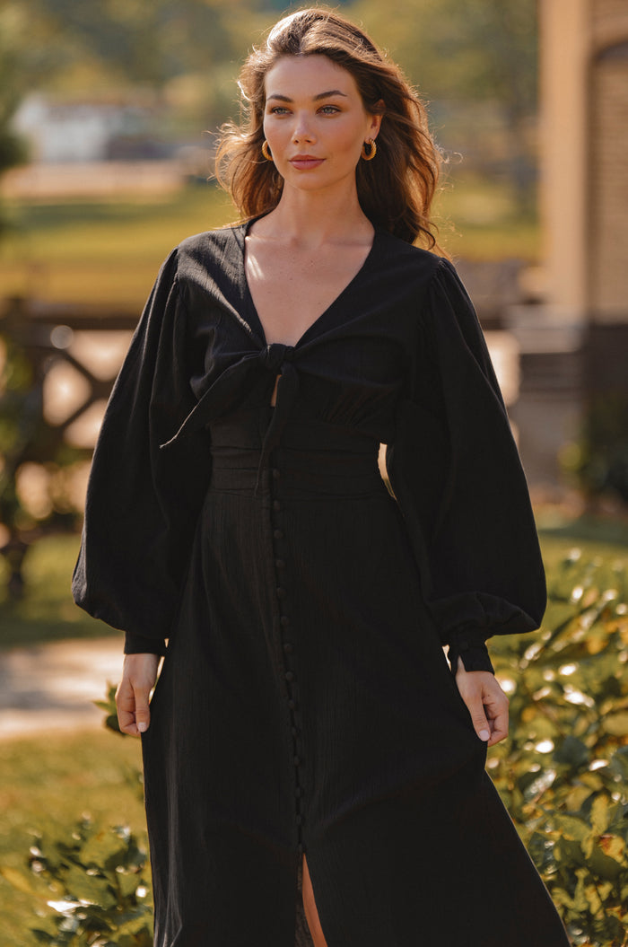 Woman wearing a black dress with a blurred outdoor background