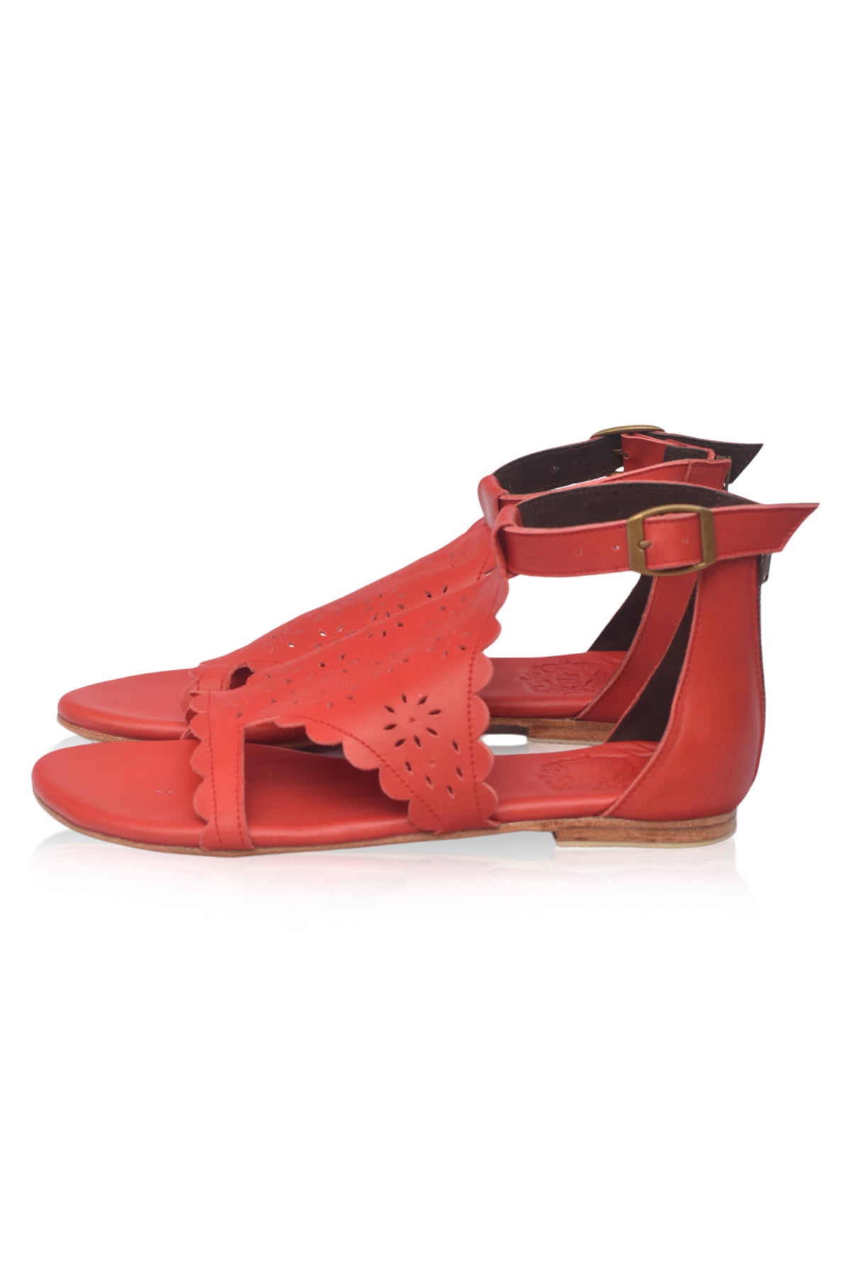 A pair of red flat sandals with cutout details on the toe strap and an adjustable ankle strap with a small gold-tone buckle, shown against a plain white background.
