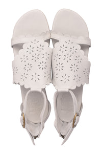 A pair of white leather sandals with scalloped edges and laser-cut floral patterns on the straps, shown from a top-down view on a white background.