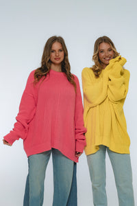Two women wearing oversized sweaters, one pink and one yellow, on a white background.