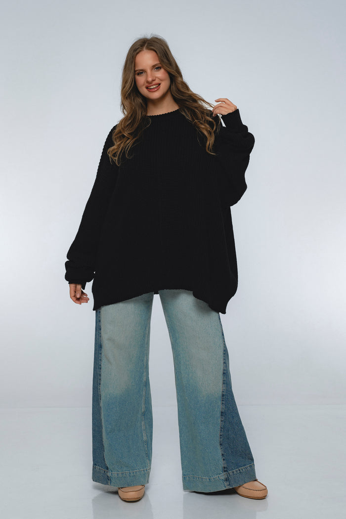Woman wearing a black oversized sweater and light blue jeans on a white background