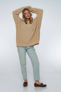 Woman wearing a beige sweater and light blue jeans on a white background