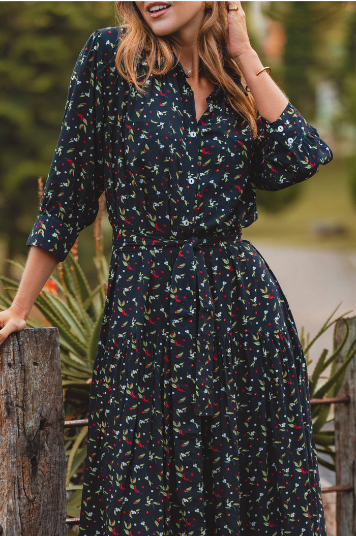 Woman wearing a dark floral dress standing outdoors with greenery in the background