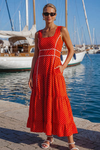 Woman in a red polka dot dress standing by a marina with sailboats.