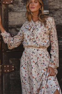 Woman wearing a floral dress standing against a wooden wall.