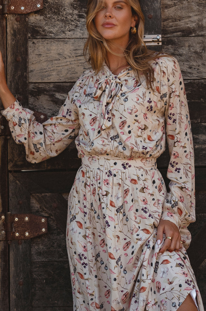 Woman wearing a floral dress standing against a wooden wall.