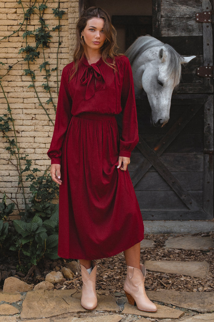 Woman in a red dress standing in front of a horse in a stable with horse