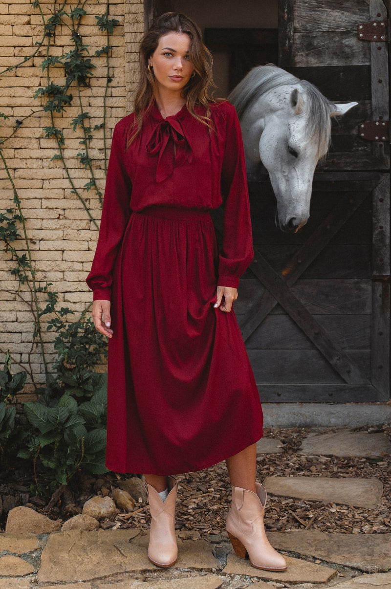 Woman in a red dress standing in front of a horse in a stable with horse