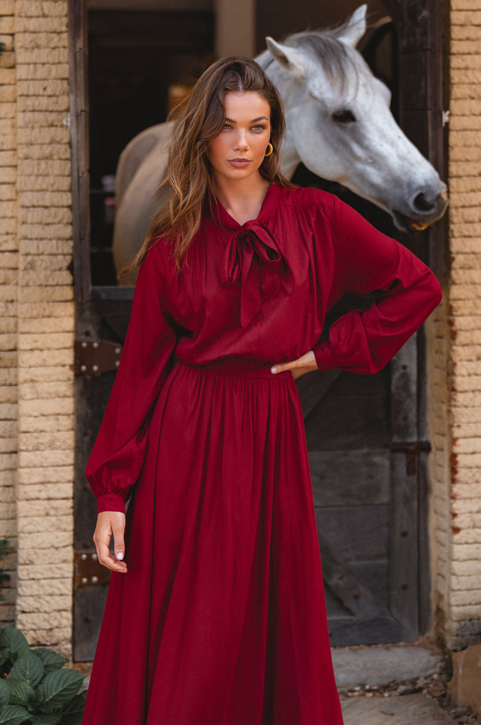 Woman in a red dress standing next to a horse in an outdoor setting.