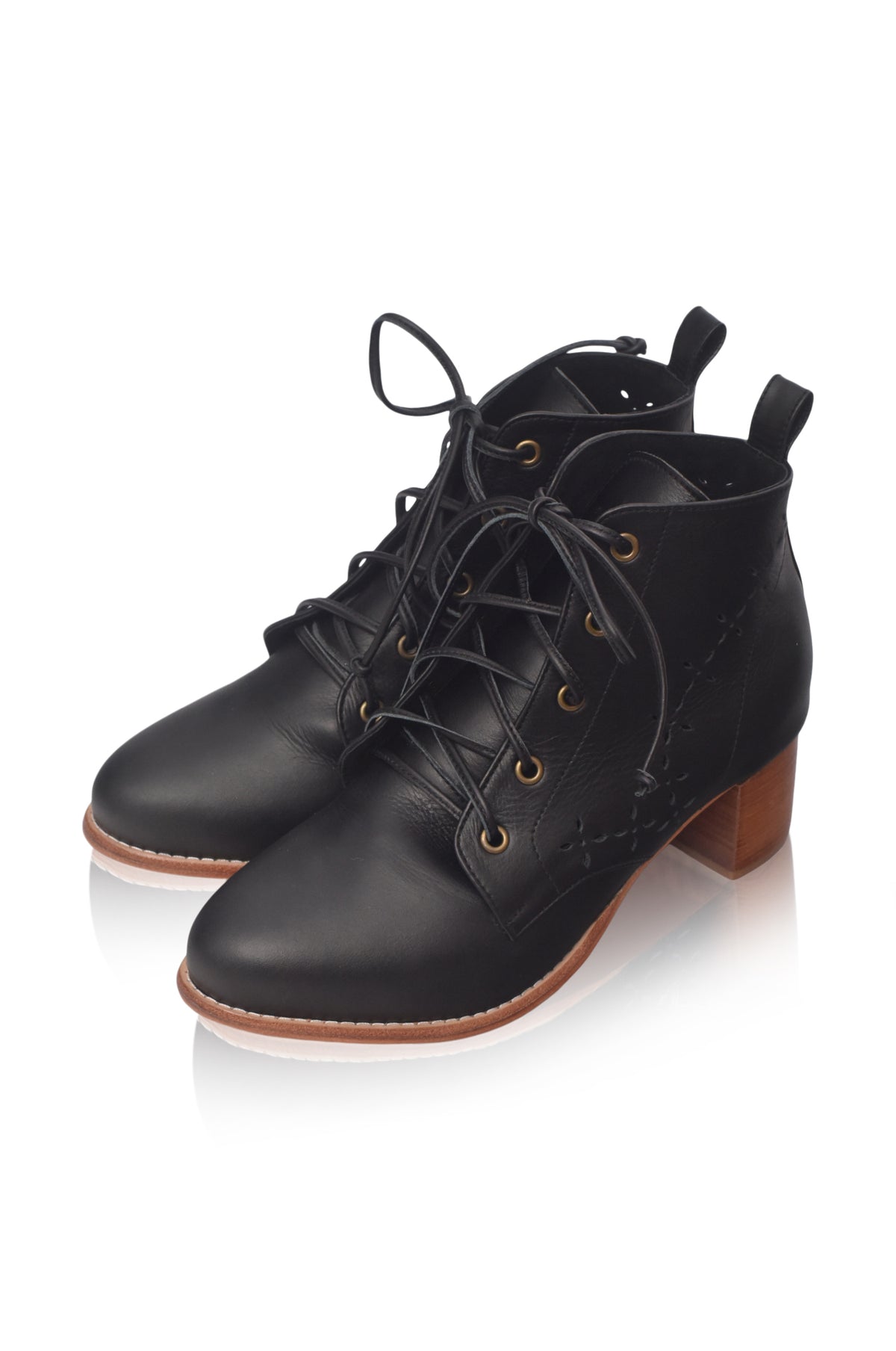 A pair of black leather lace-up ankle boots with low block heels, gold eyelets, and brown soles, shown on a white background with a soft reflection.