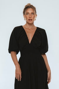 Woman wearing a black dress with puff sleeves against a white background