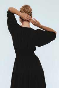 Person wearing a black dress with wide sleeves against a white background