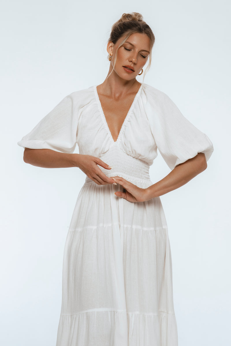 Woman wearing a white dress with flutter sleeves on a plain background