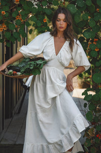 Woman in a white dress holding a tray of vegetables amidst greenery
