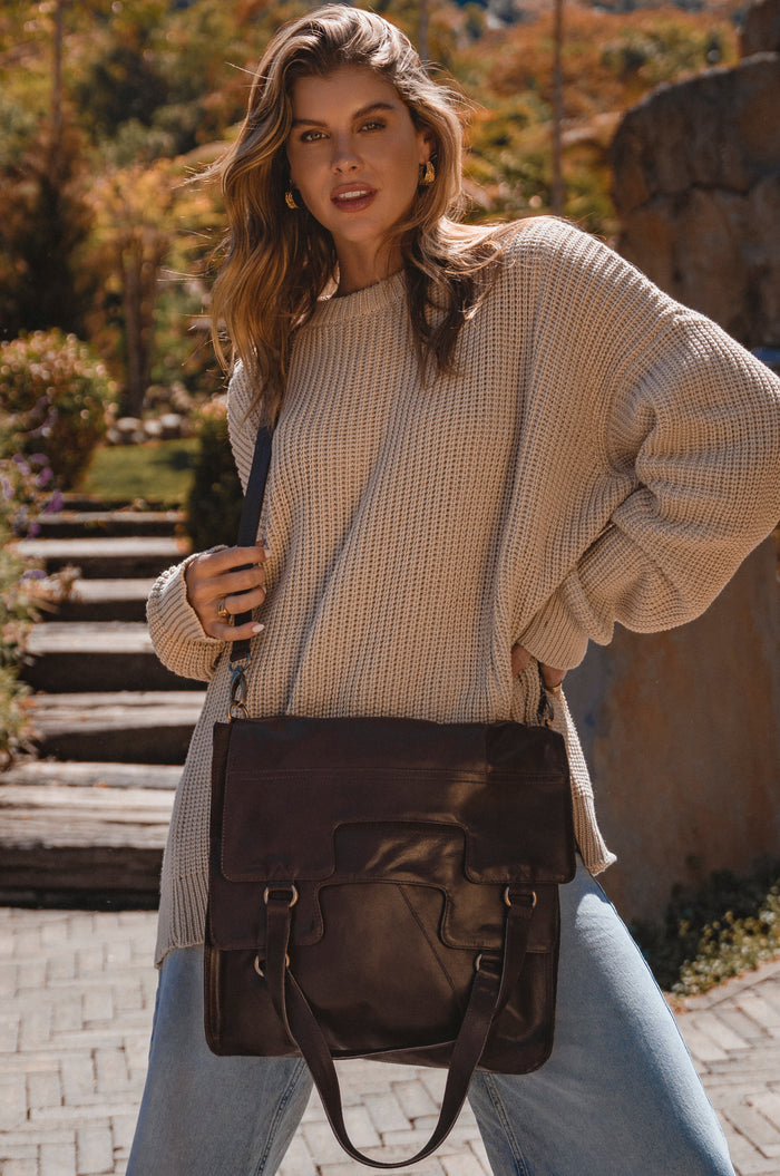 Woman holding a brown leather bag in an outdoor setting