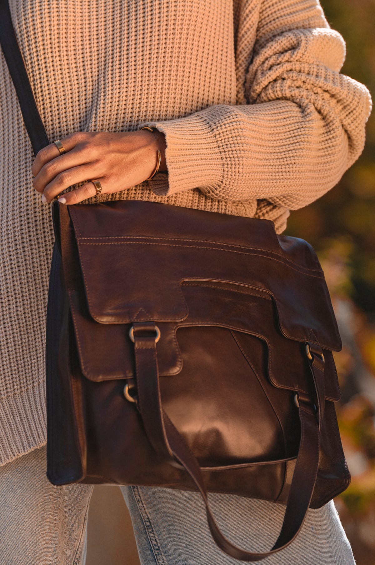 Brown leather bag held by a person wearing a beige sweater and jeans.