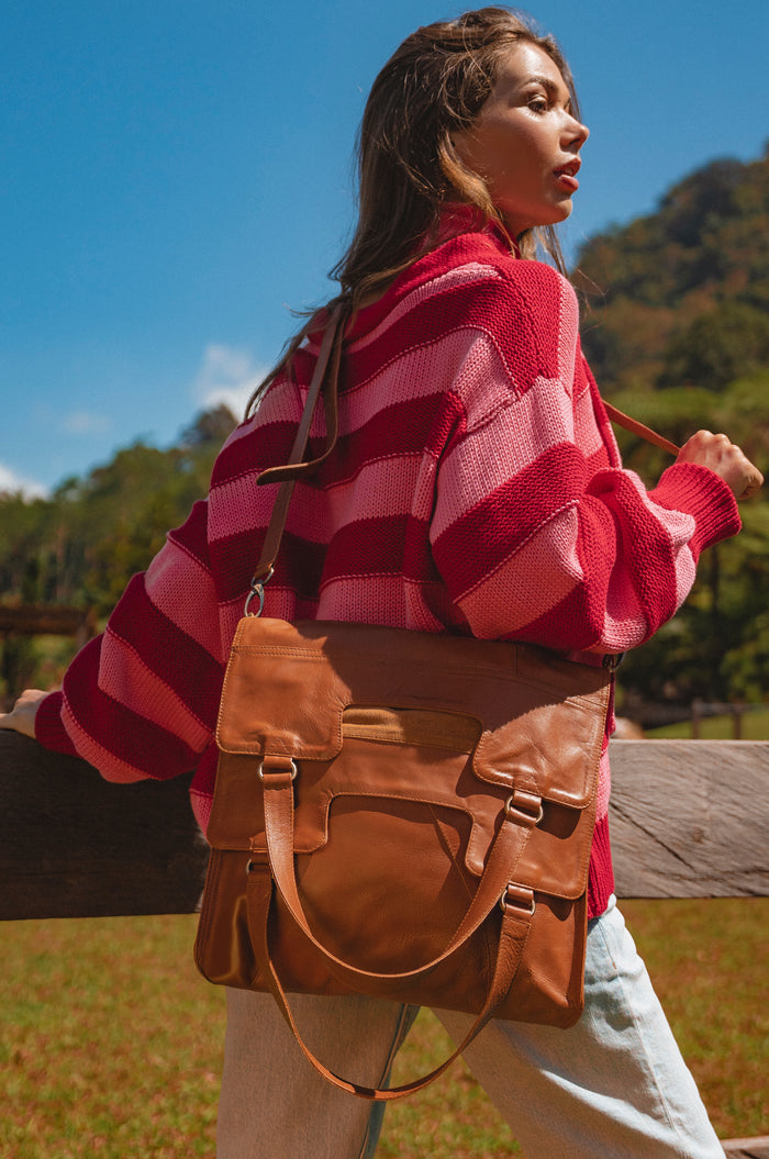 Woman in a red and pink striped sweater with a brown leather bag outdoors.