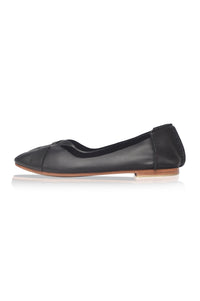 A single black leather ballet flat shoe with a pointed toe and a light brown wooden-look sole, shown in profile against a white background.