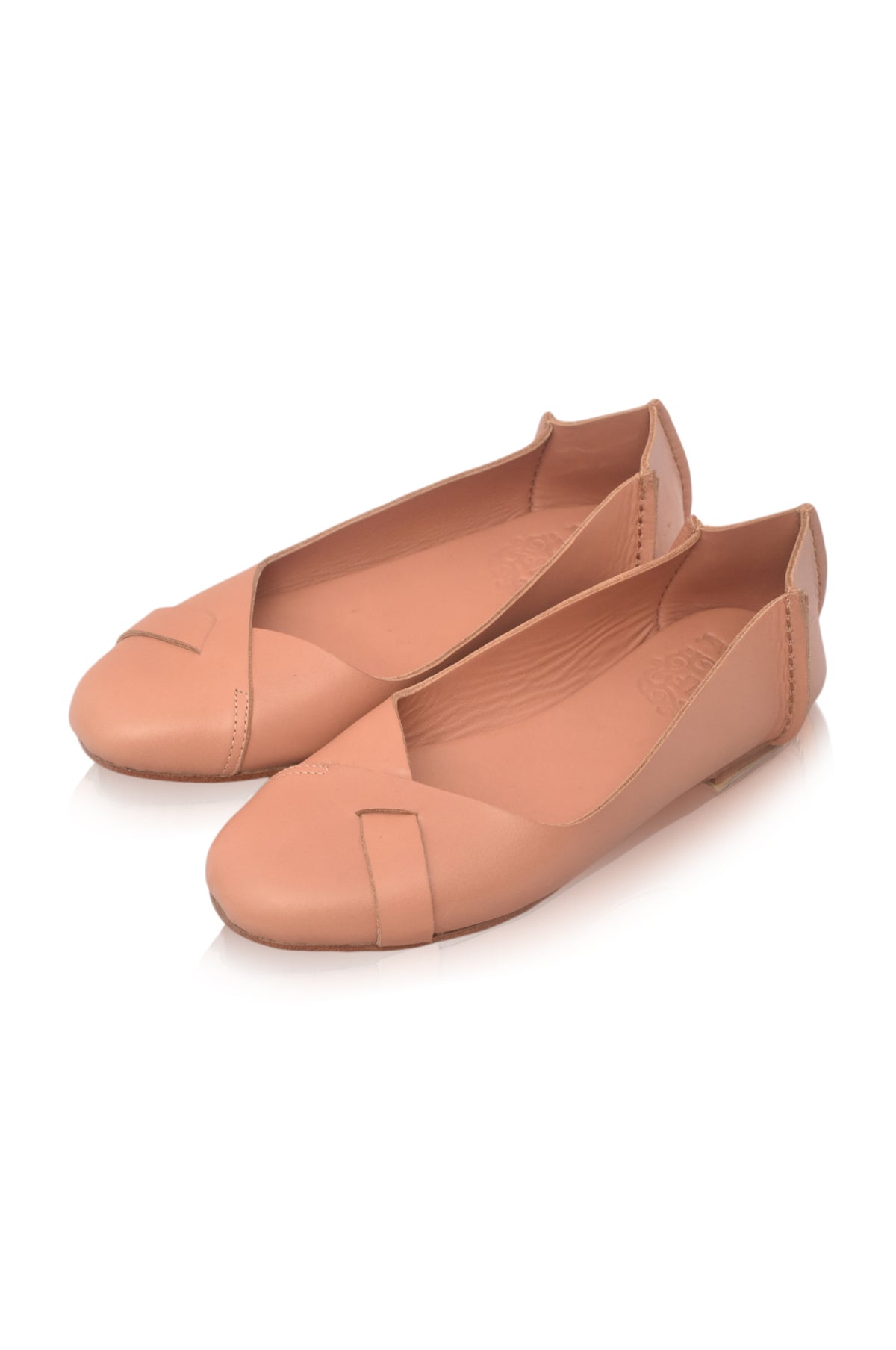 A pair of women's flat shoes in a warm peach-beige color, featuring a crossover strap design across the toes, shown on a clean white background.