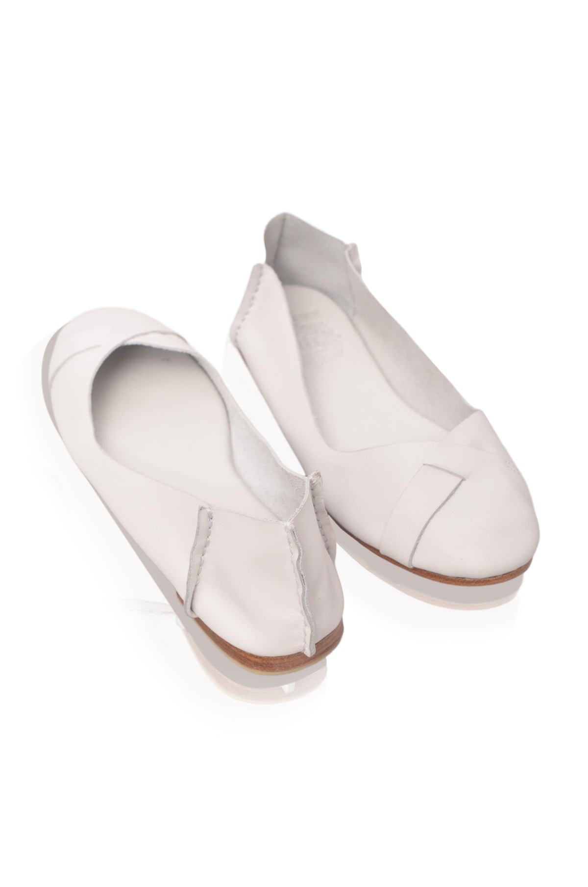 A pair of off-white leather slip-on flats with a pointed toe and decorative stitching, displayed on a clean white background.