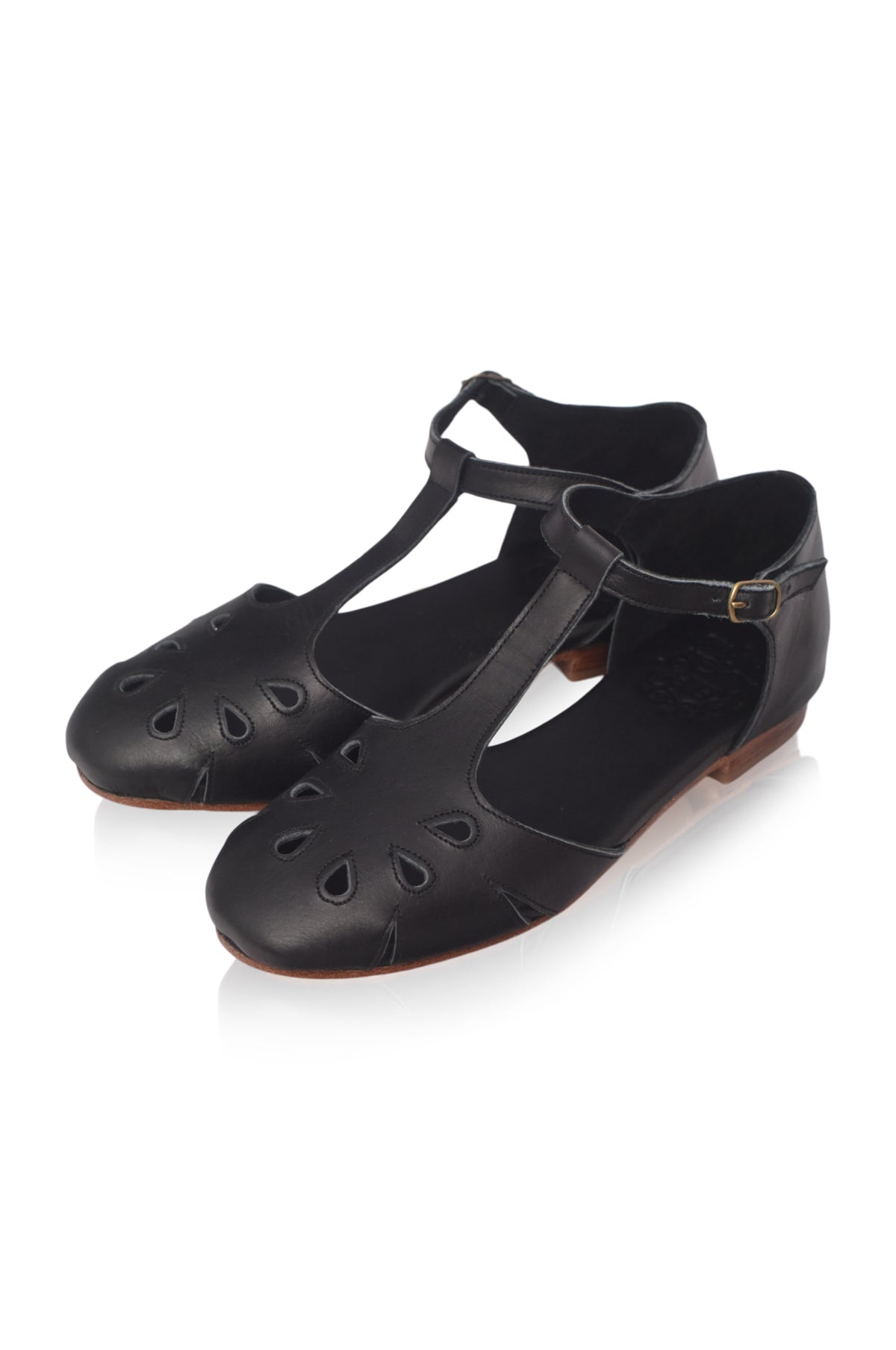 A pair of black leather T-strap Mary Jane flats with decorative cutouts on the toe, shown on a clean white background.