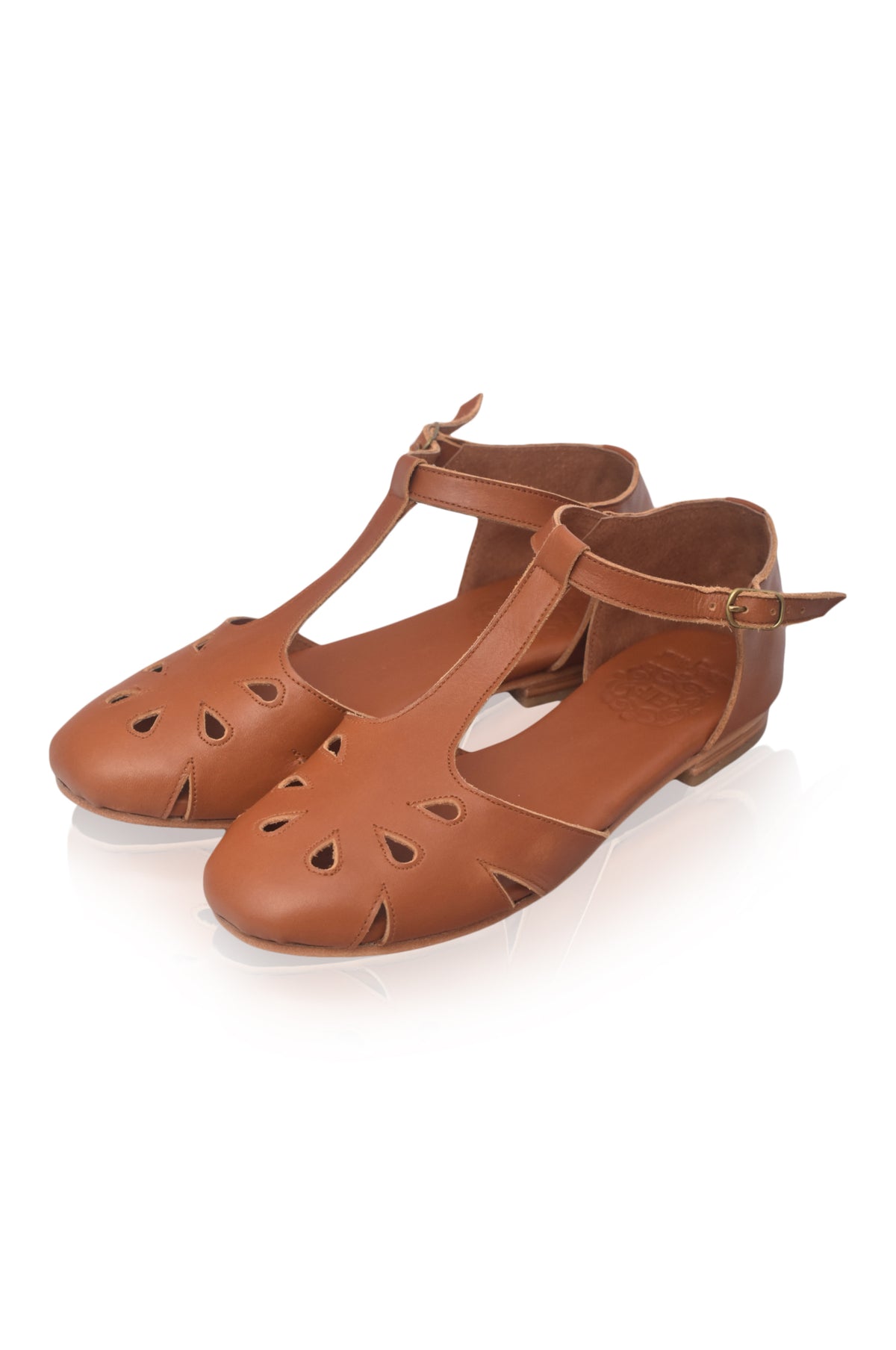 A pair of brown leather T-strap flat shoes with decorative cutouts on the toe, displayed on a clean white background.