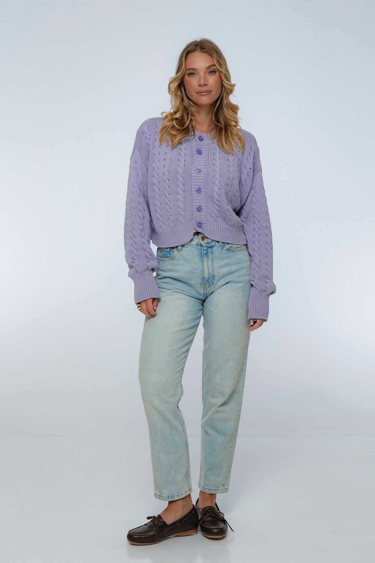Woman wearing a purple textured sweater and light blue jeans on a white background