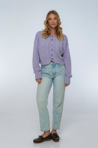 Woman wearing a purple textured sweater and light blue jeans on a white background