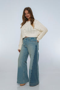 Woman wearing a cream sweater and blue jeans on a white background