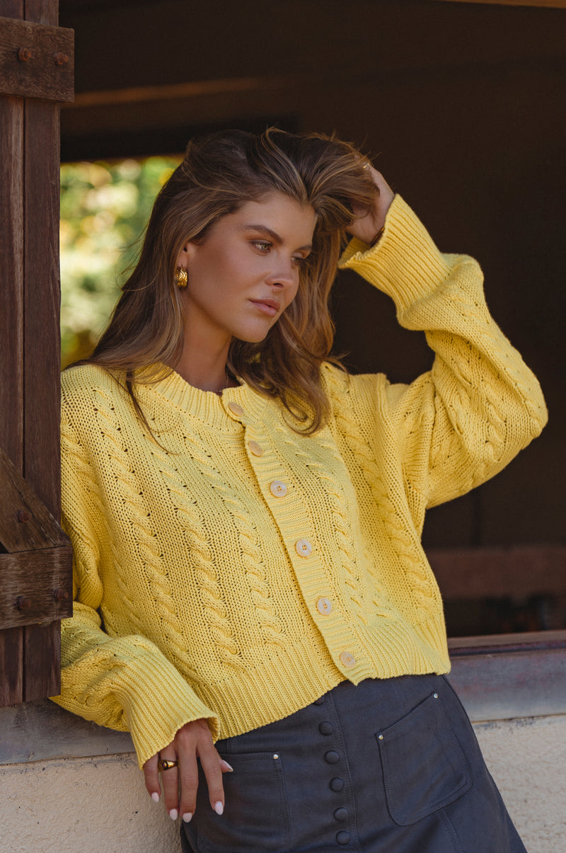 Woman wearing a yellow knitted cardigan standing outdoors.