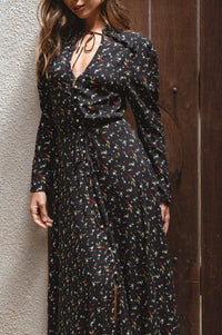 Woman wearing a black floral dress against a textured wall and wooden door.