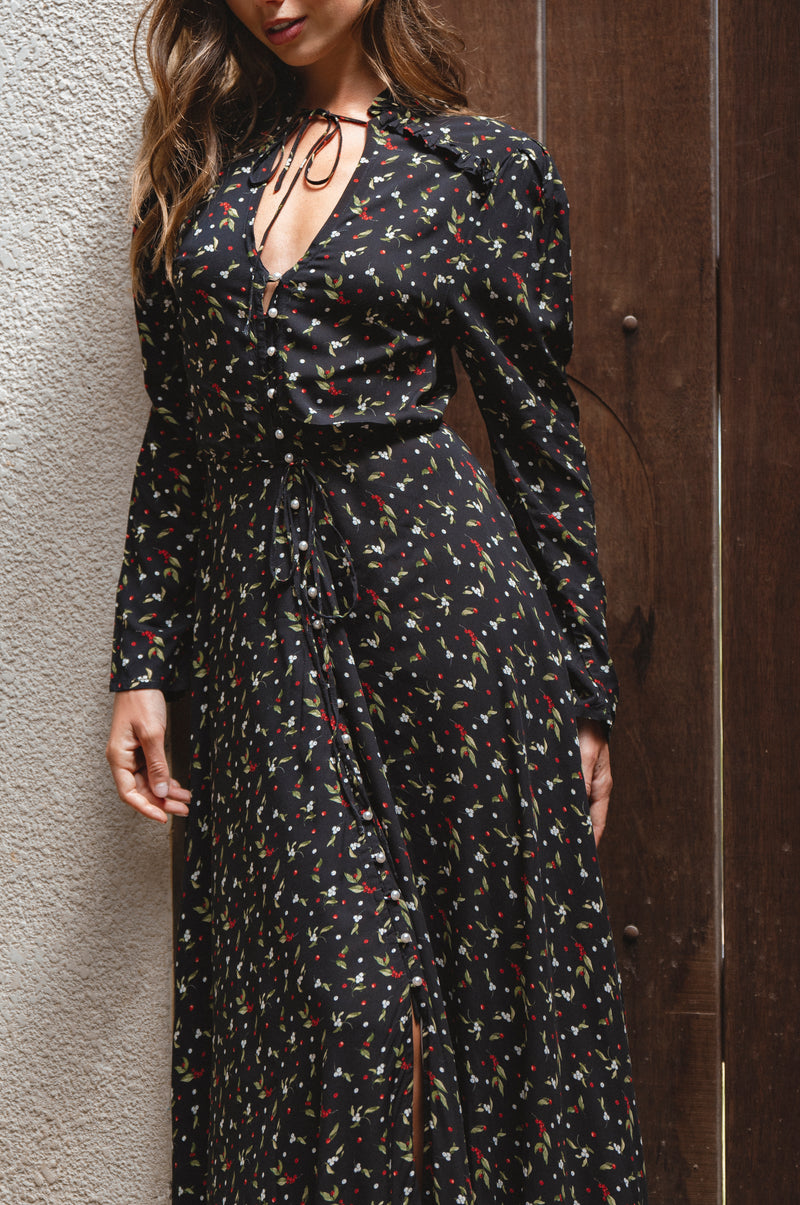 Woman wearing a black floral dress against a textured wall and wooden door.