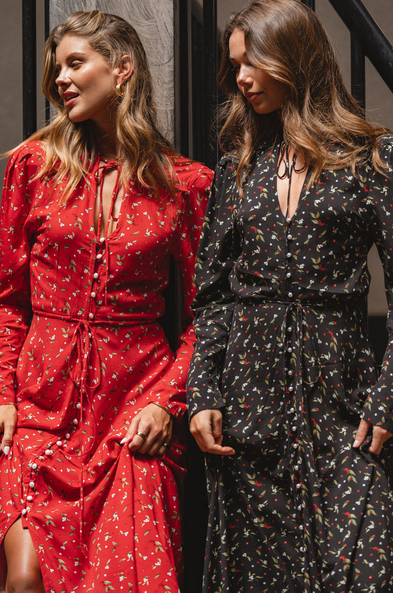 Two women wearing red and black floral dresses standing next to each other.