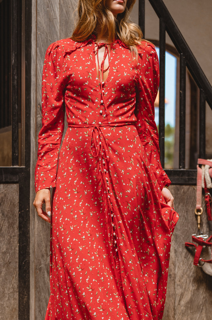 Woman wearing a red floral dress standing outdoors.