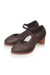 A pair of dark brown leather Mary Jane-style block heel shoes with ankle straps and a small gold-tone buckle, displayed on a clean white background.