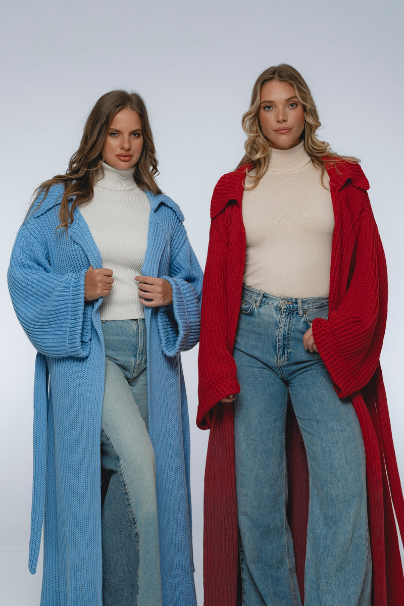 Two women wearing long cardigans, one blue and one red, standing side by side against a white background.