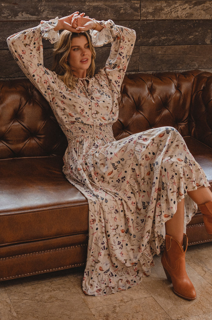 Woman in a floral dress sitting on a brown leather couch with a wooden wall background